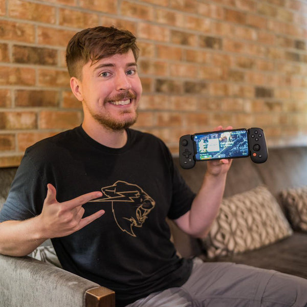 Mr. Beast holding a smartphone with a gaming app on it, sitting in a living room.