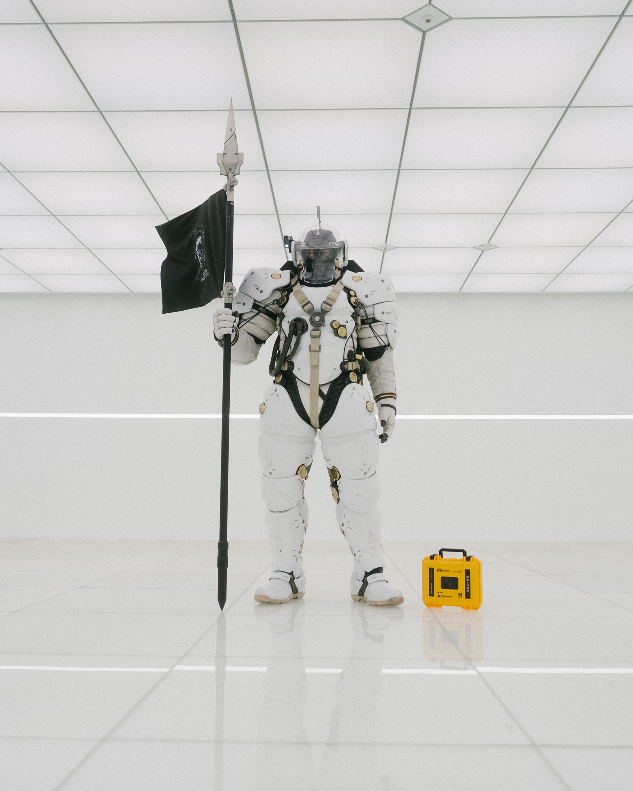 Person in a futuristic suit holding a flag in a white room with a yellow device on the floor.